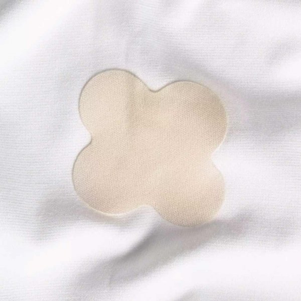 En ljust beige självhäftande laglapp på ett vitt tyg.