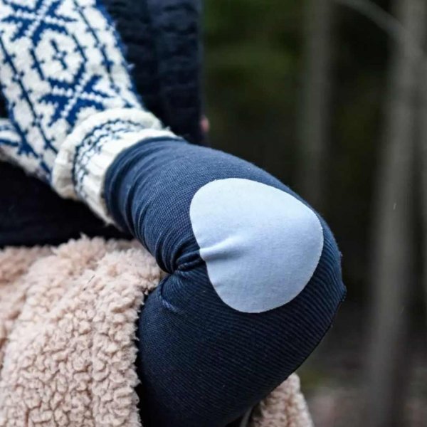 En grå armbågslapp i 100% merinoull på en blå tröja.