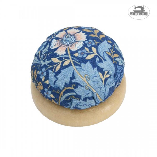 En snygg stoppad nåldyna med blått tyg med blommor och en stabil träbotten.