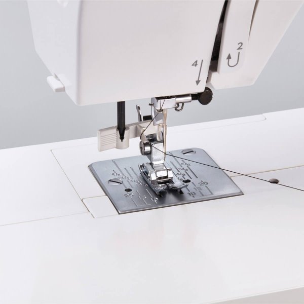 Närbild på nålområdet på Janome 1522BG Blue Grey, som visar den mekaniska nålpåträdaren i sänkt läge vid nålsögat med en svart s