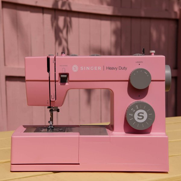 Rosa symaskin Singer Heavy Duty HD4411 placerad utomhus på ett trábord framför ett rosa plank.